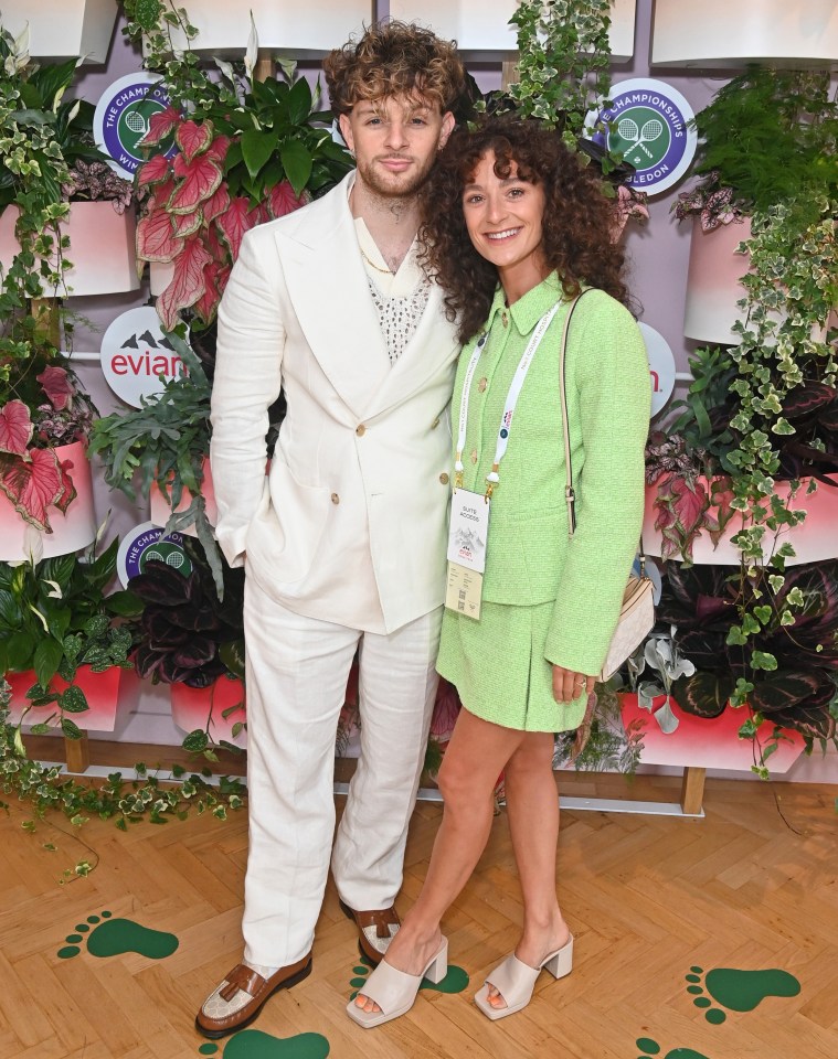 a man in a white suit and a woman in a green dress pose for a photo