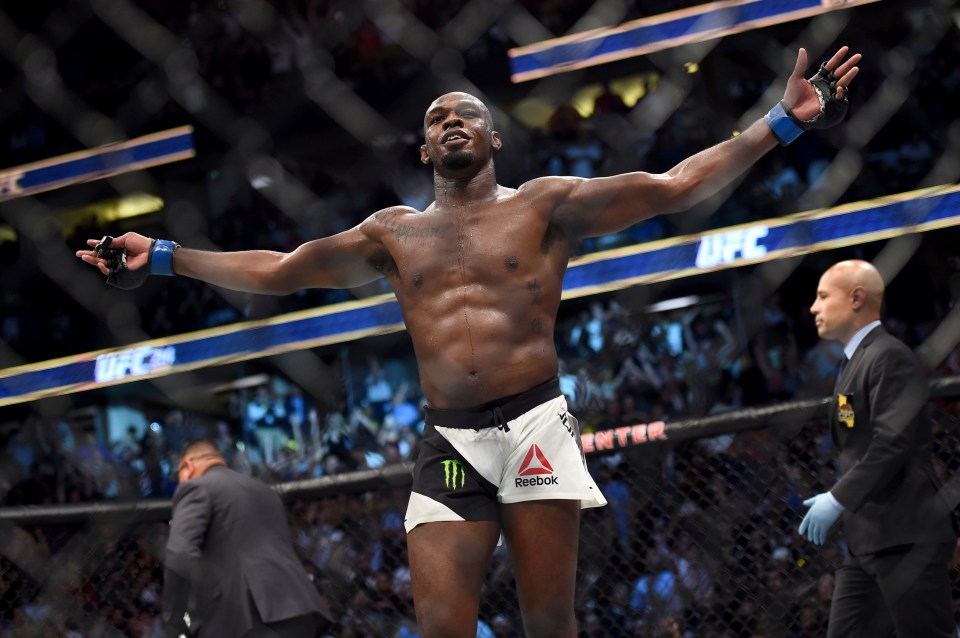 a man in reebok shorts stands in a cage with his arms outstretched