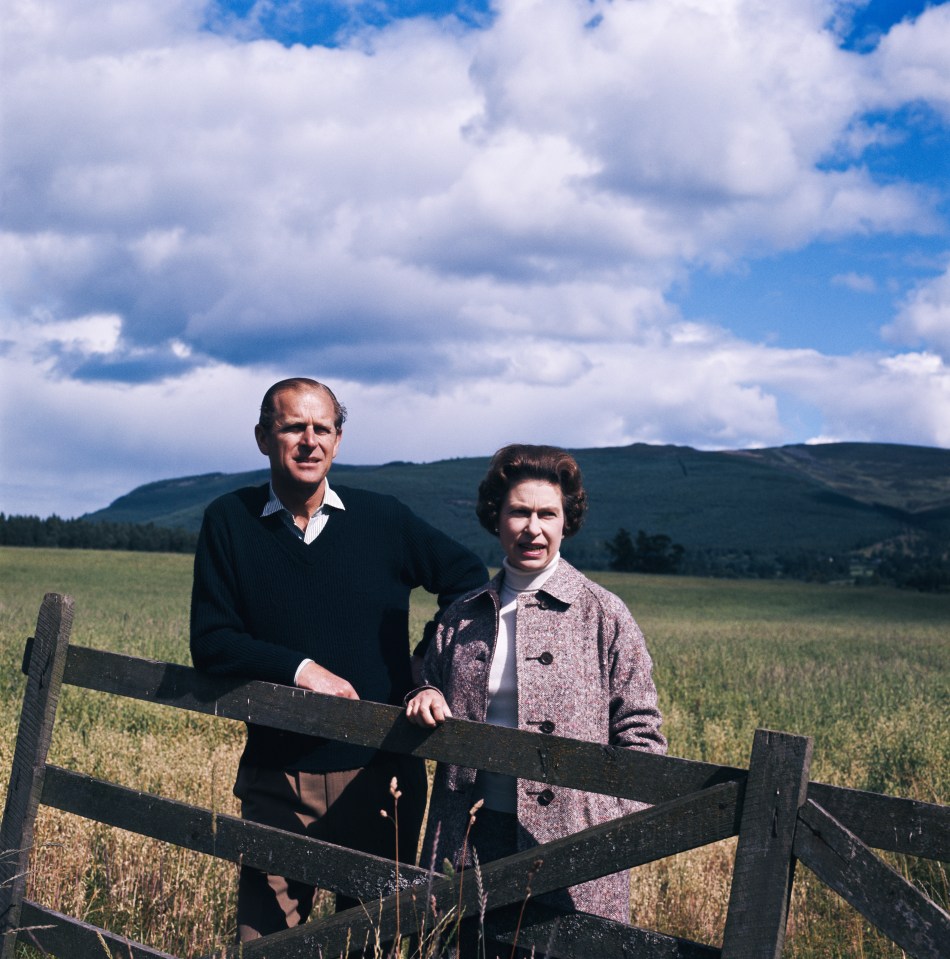 a man and woman standing next to a wooden fence in a field