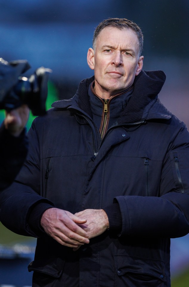a man in a black jacket stands with his hands folded