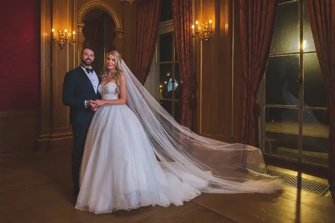 the bride and groom are posing for a picture in a room with a long veil blowing in the wind .