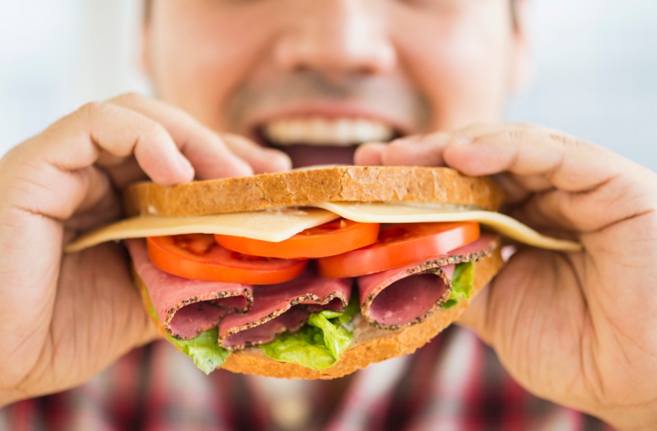 a man is eating a sandwich with meat cheese and tomatoes