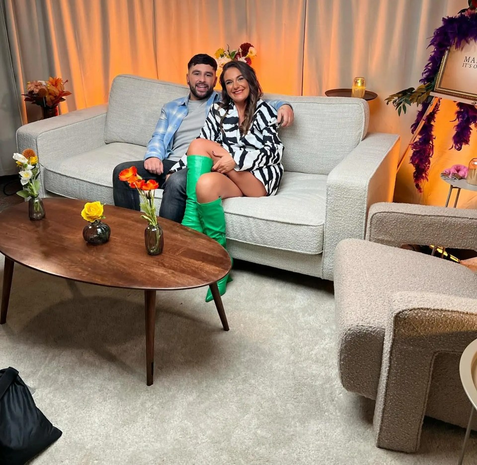 a man and woman sit on a couch in front of a sign that says max factor