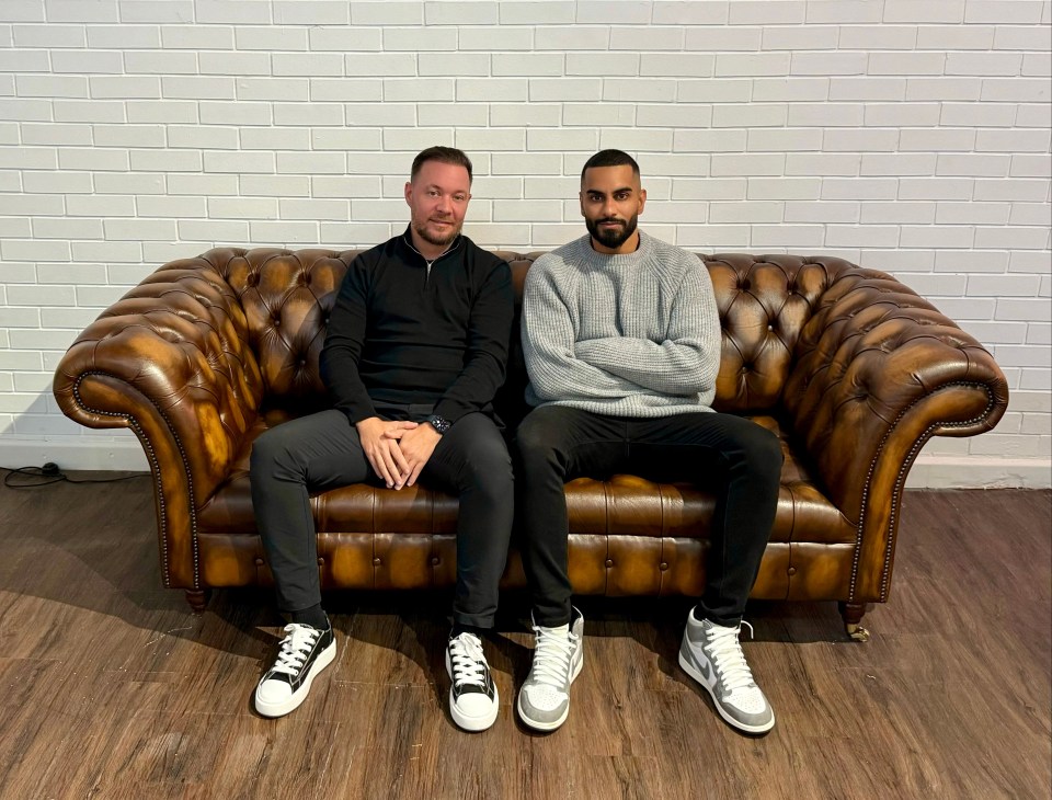 two men sit on a couch with their arms crossed