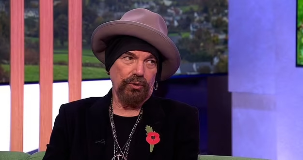 a man with a beard and a hat is sitting on a couch .
