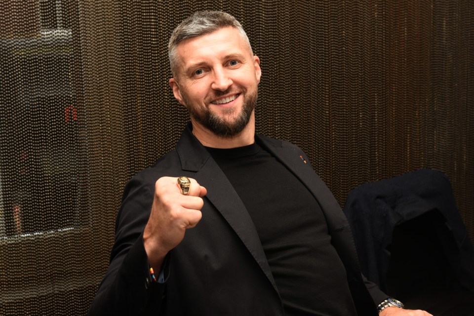 a man in a black suit holds up a gold ring