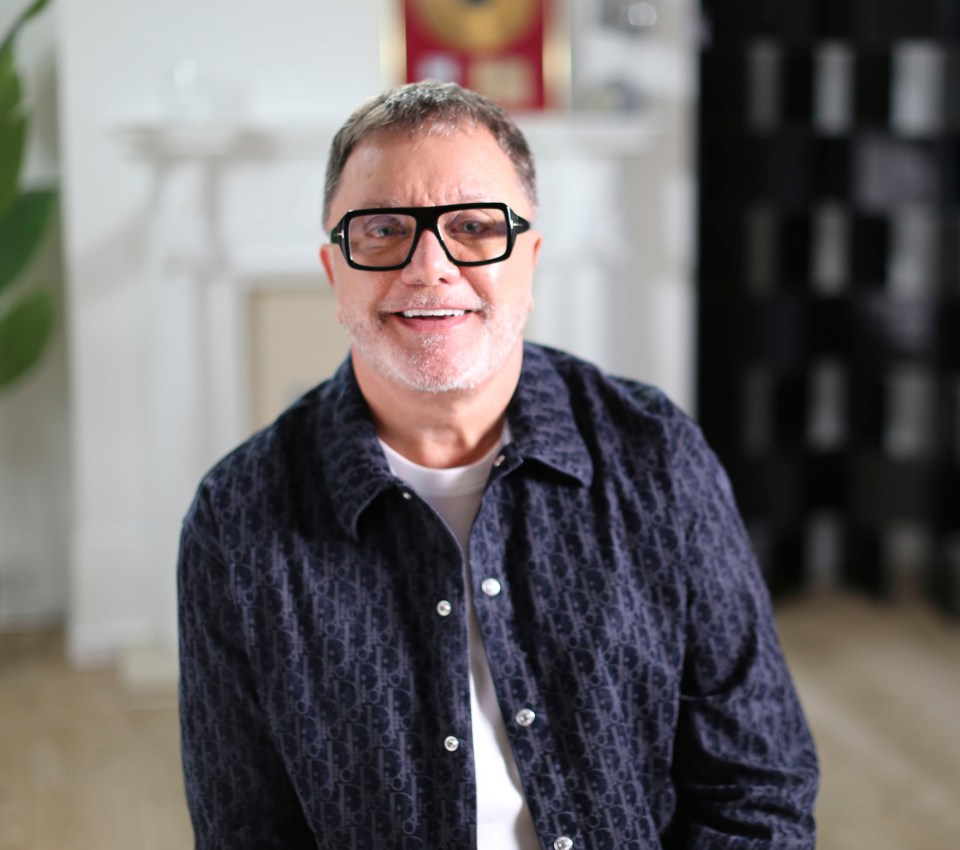 a man wearing glasses and a dior shirt smiles for the camera