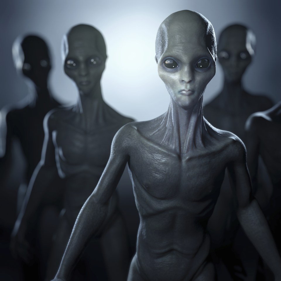 a group of grey aliens are standing in a dark room