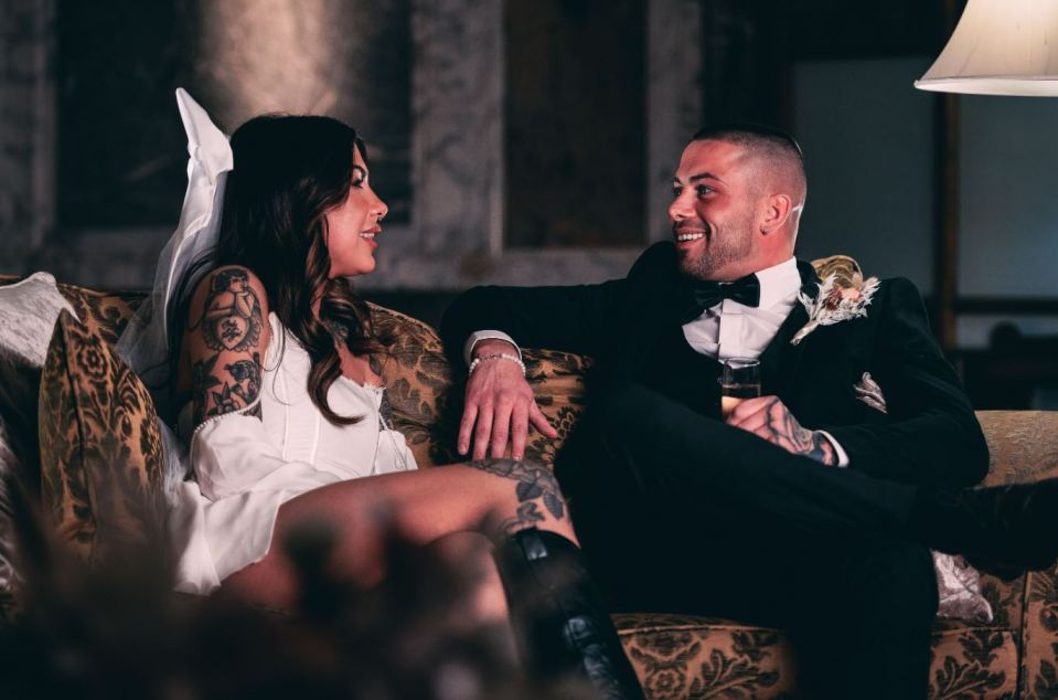 a bride and groom sit on a couch looking at each other