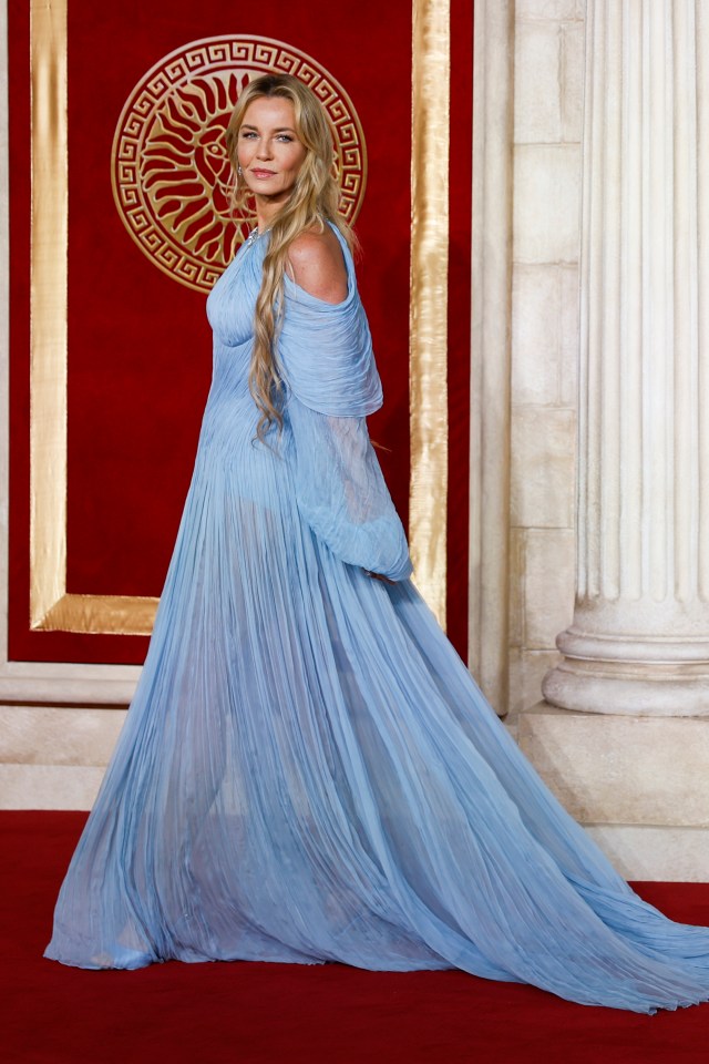 a woman in a long blue dress is standing on a red carpet