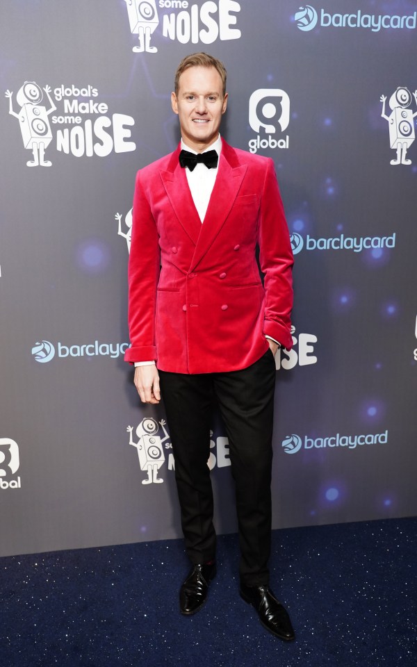 a man in a red suit stands in front of a wall that says global 's make some noise