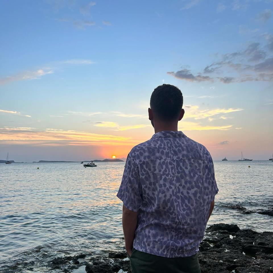 a man in a leopard print shirt looks at the sunset over the ocean