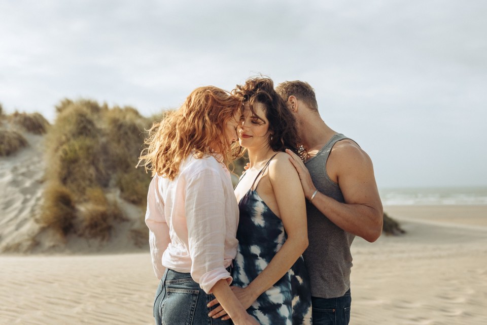 a man and two women standing on a sandy beach