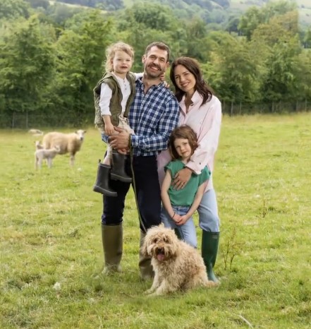 a family is posing for a picture in a field with sheep in the background .