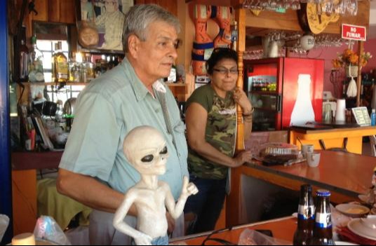 Man and woman at a bar with an alien figurine.