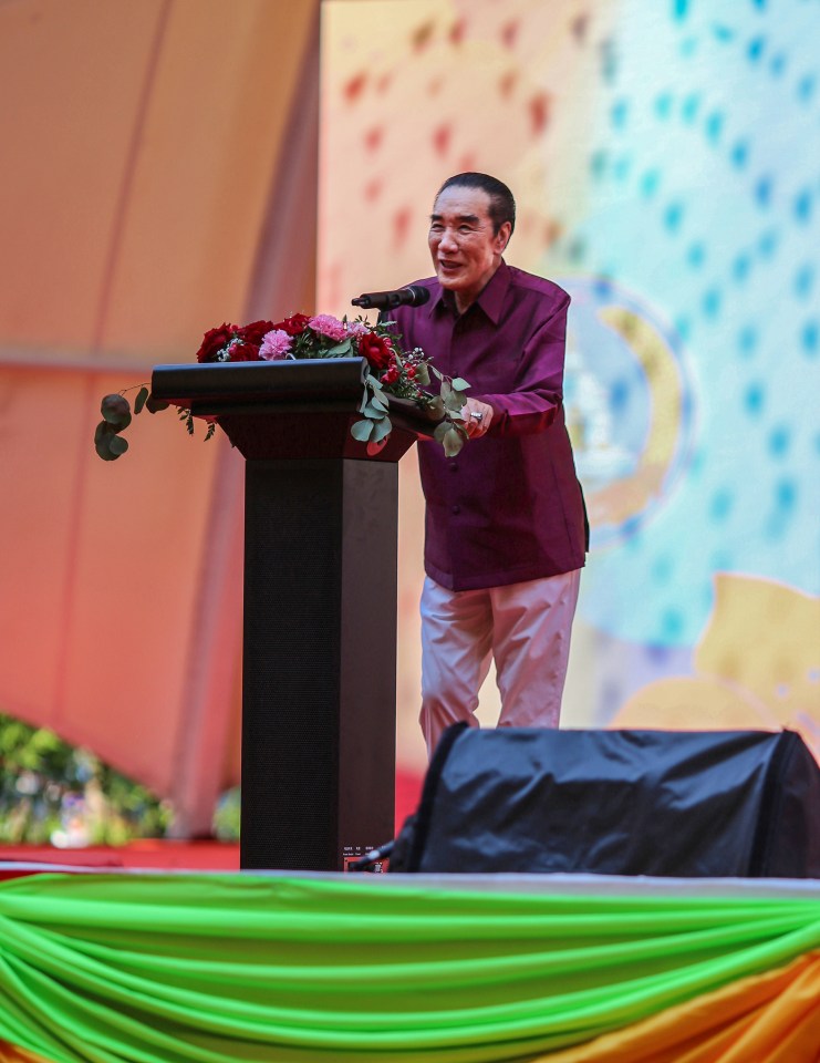 a man in a purple shirt stands at a podium with flowers on it
