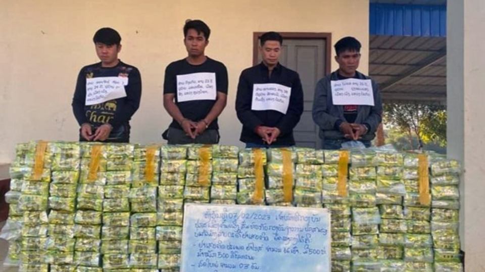 four men are standing in front of a stack of bags with one of them wearing a shirt that says har