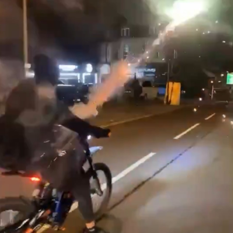 a person is riding a bike down a street at night while holding a firework .