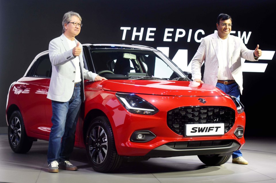 two men stand in front of a red swift car
