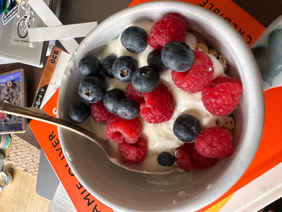 a bowl of yogurt with raspberries and blueberries sits on top of a book by annie oliver