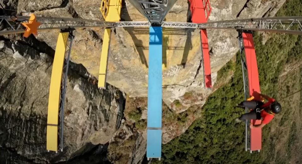 a man in a red shirt is hanging from a colorful bridge