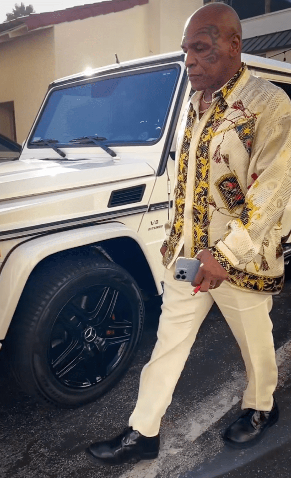 a man with a tattoo on his face stands in front of a white mercedes
