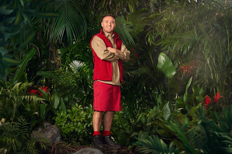 a man in a red vest stands in a jungle with his arms crossed