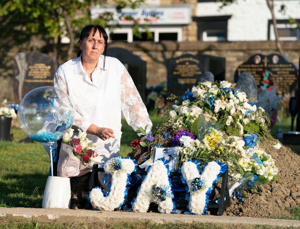 A woman mourns at a gravesite decorated with flowers and a balloon that says "Rest In Peace Jay."