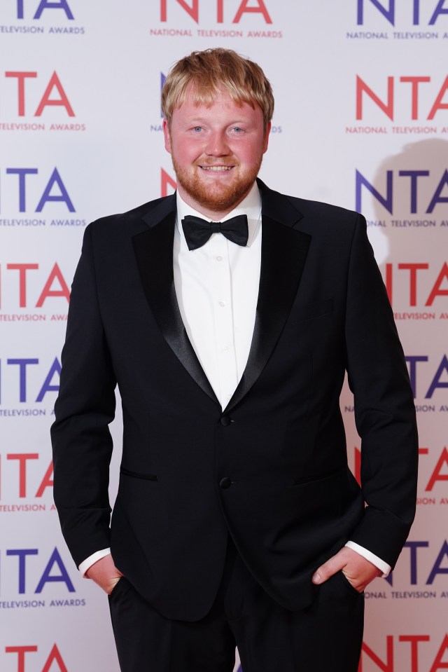 a man in a tuxedo stands in front of a wall that says national television awards