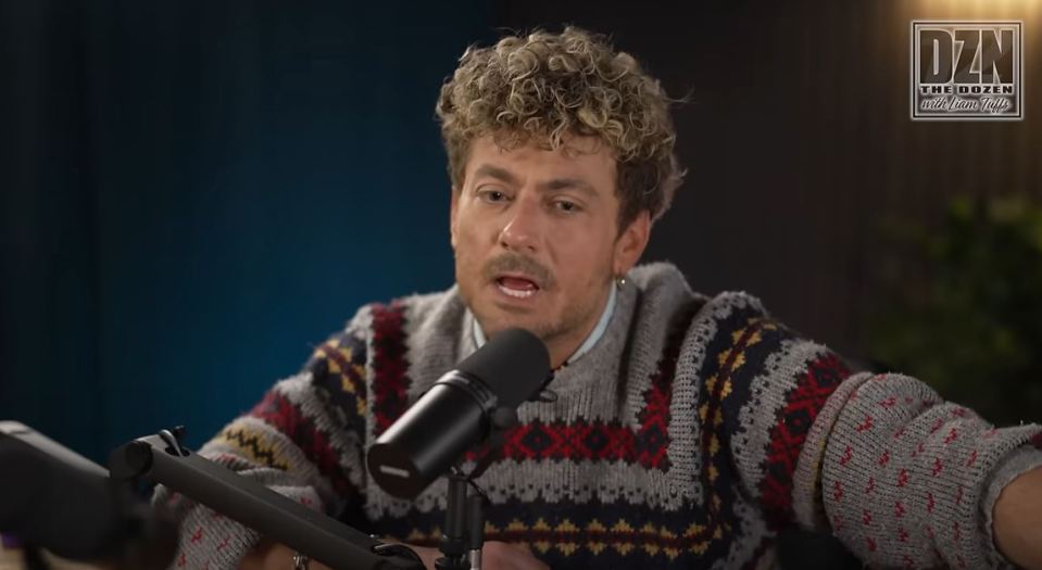 a man in a sweater is speaking into a microphone with the dzn logo behind him