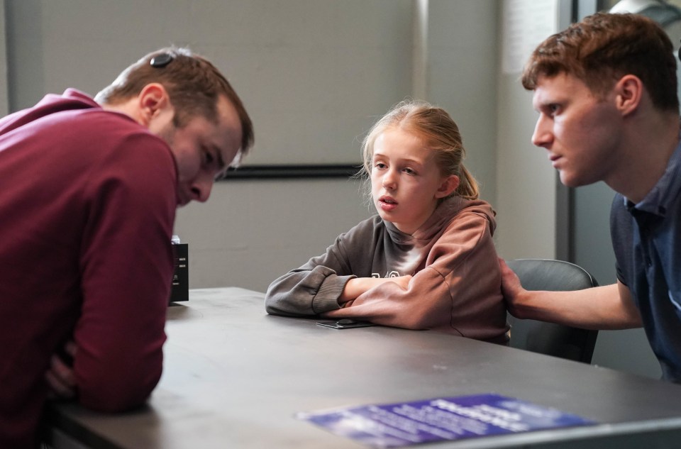 a little girl sits at a table with two men