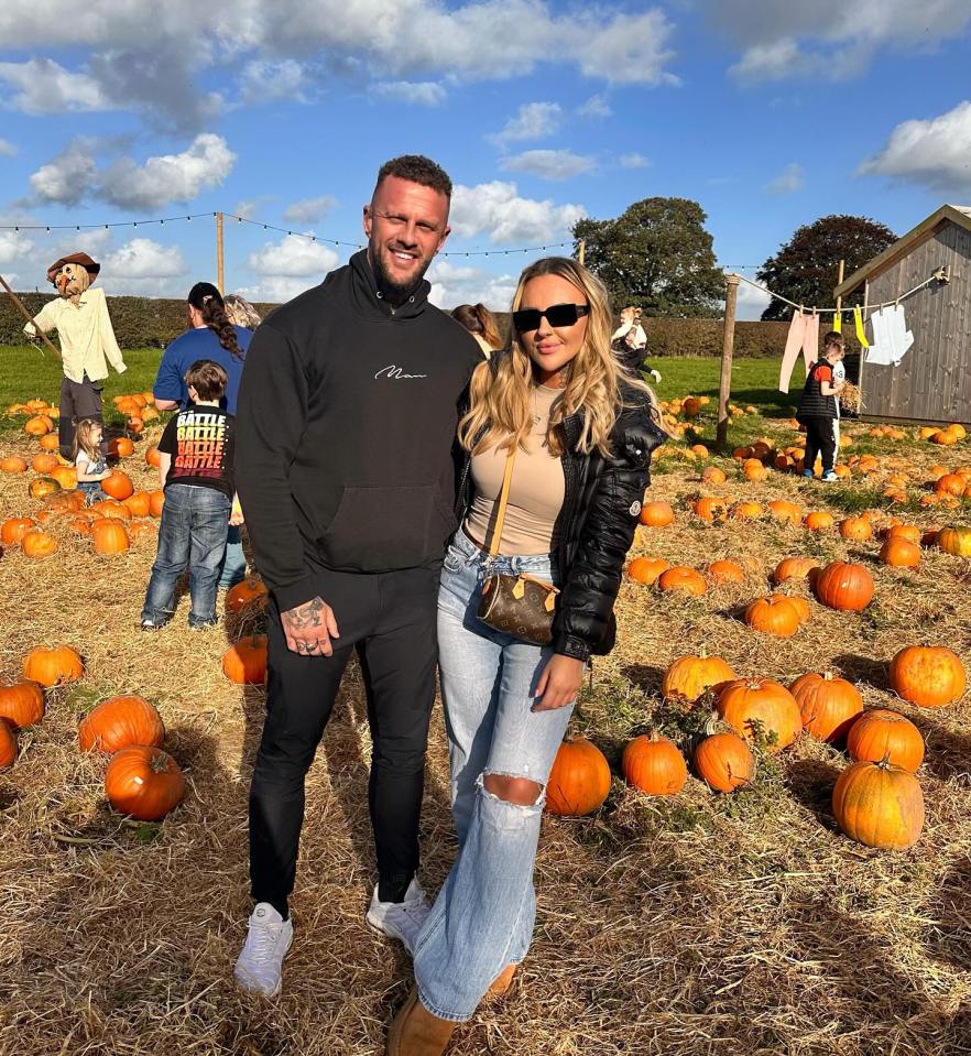 a man and woman standing in a field of pumpkins with a scarecrow in the background