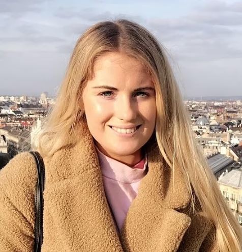 a woman in a brown coat is smiling in front of a city .