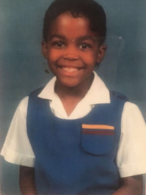 a young boy in a blue vest and white shirt smiles for the camera