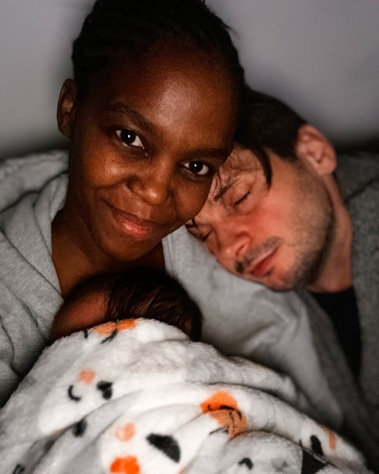 a woman holds a baby while a man sleeps next to her