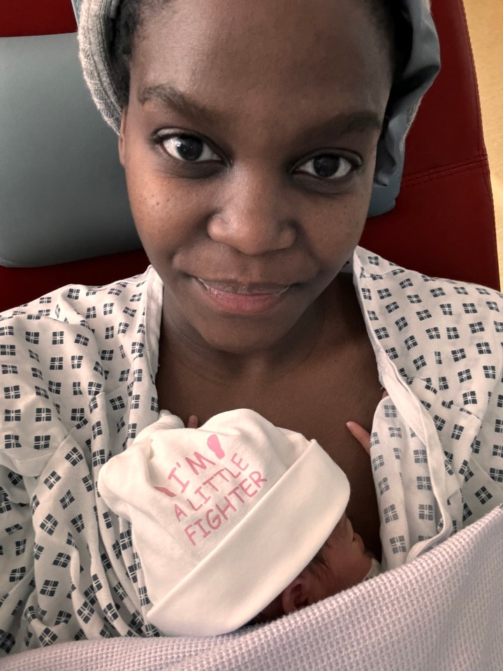 a woman in a hospital gown is holding a baby wearing a hat that says i 'm a little fighter
