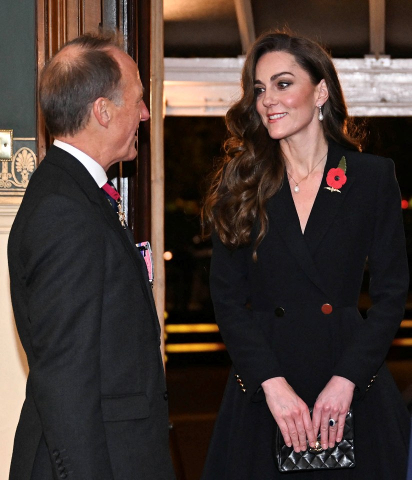 a woman in a black jacket has a poppy pin on her jacket