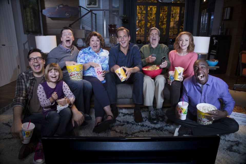 a group of people are sitting on a couch eating popcorn and drinking soda