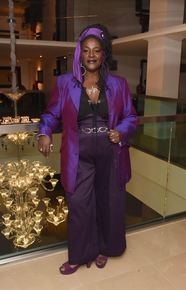 a woman in a purple suit stands in front of a chandelier