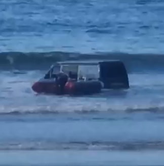 a van is stuck in the water on the beach .