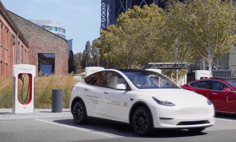 a white tesla model y is charging at a tesla charging station