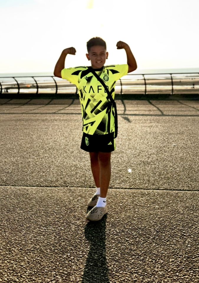 a young boy flexes his muscles while wearing a kafl shirt