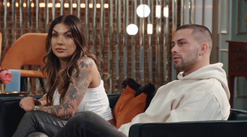 a man and a woman sit on a couch looking at something