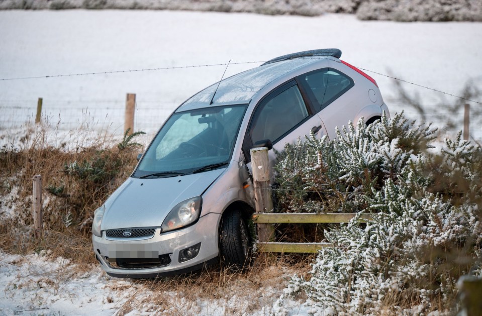 a silver ford car crashed into a fence in the snow