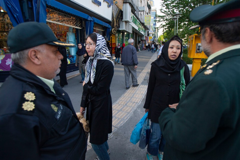 Two Iranian morality police officers speak with two women on a Tehran street.