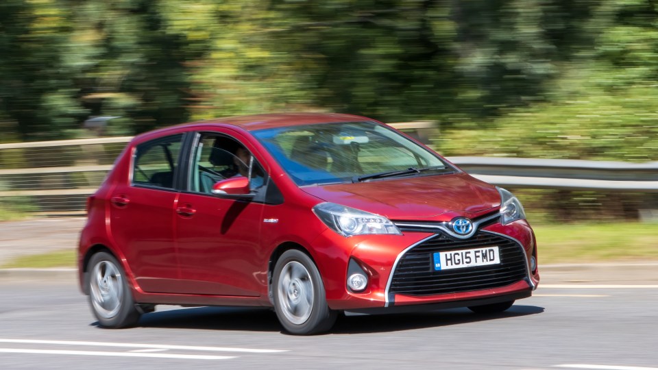 Red Toyota Yaris hybrid driving on a road.