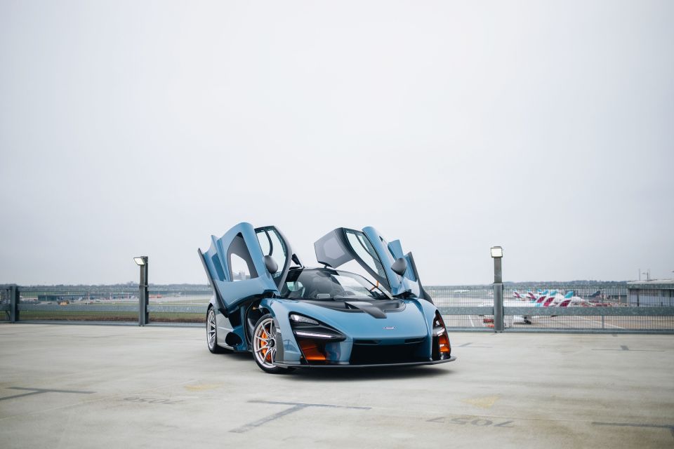 A blue McLaren Senna XP with its doors open, parked in a parking lot.