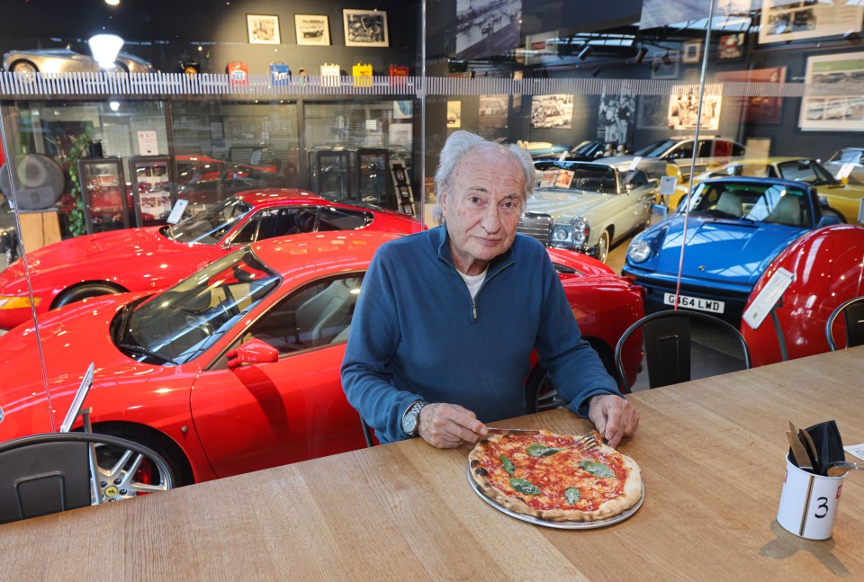 A man eats pizza in a classic car showroom.