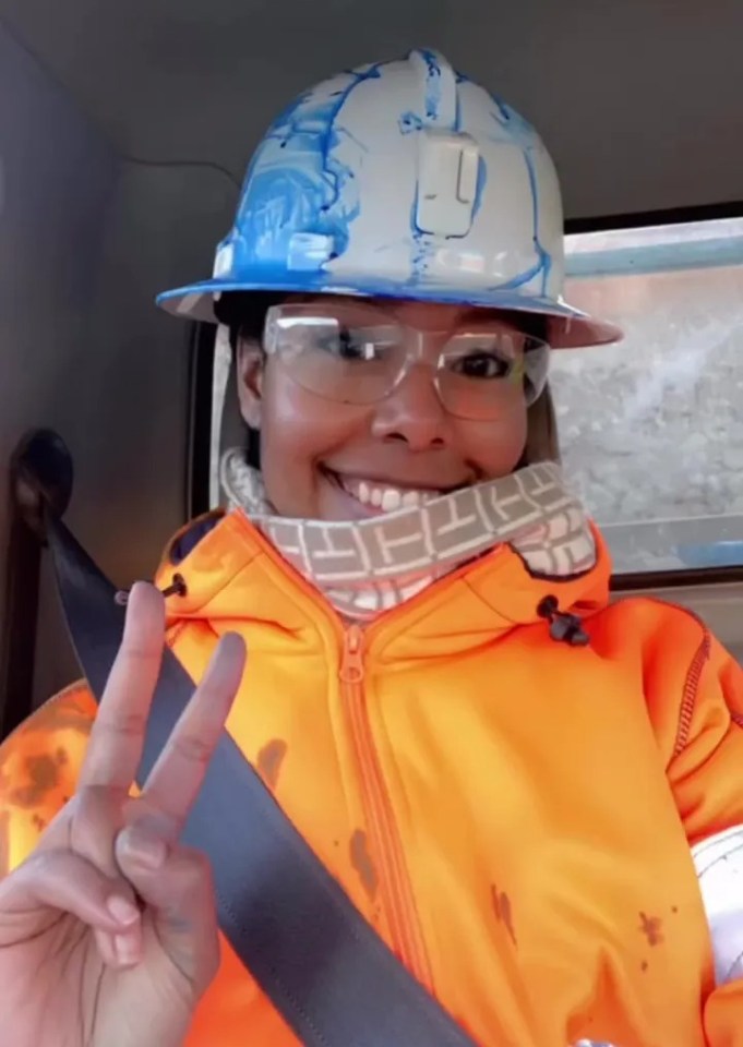 A female miner giving a peace sign while wearing safety gear in her truck.