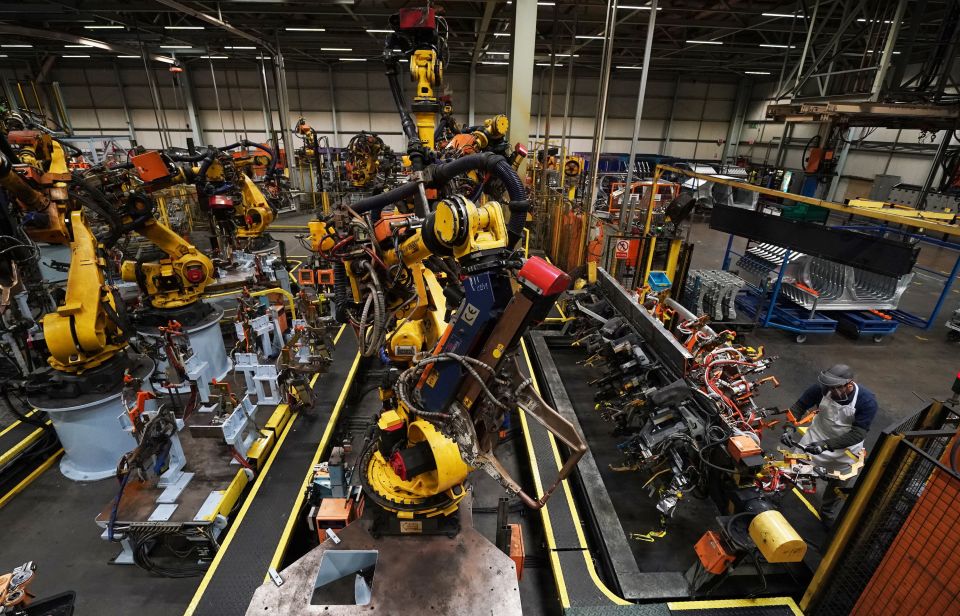 A worker monitors robotic arms assembling car parts on a factory production line.